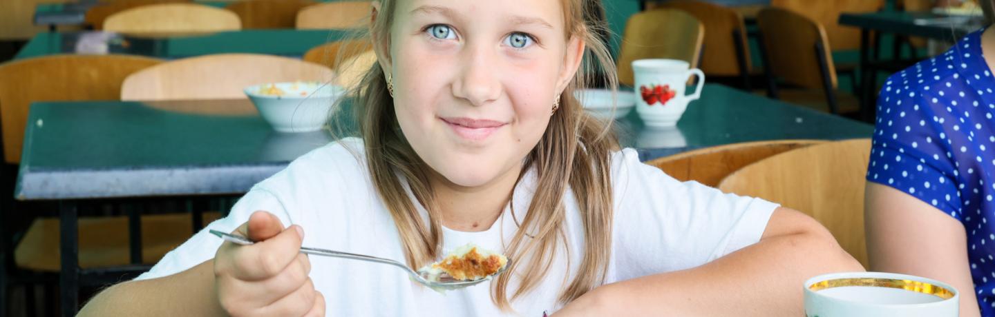 A girl at a table, smiling while holding a spoon