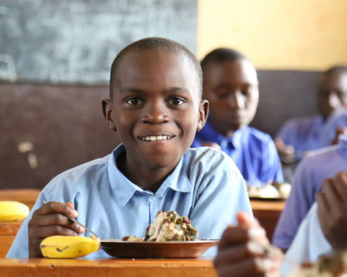 A boy happily eating a banana in a classroom