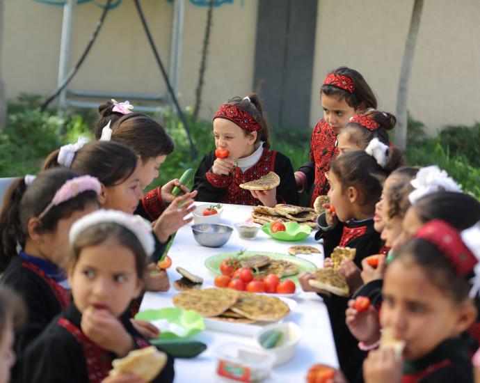 Children eating at a table outside with food.