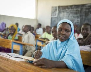 A young student sits at a desk in a classroom.